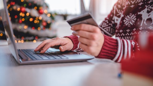 Women wearing red sweater shopping online and using credit card at home office