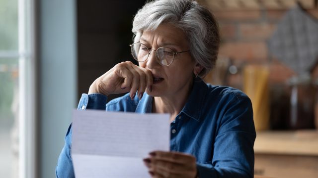 A senior woman reading a letter with a distressed look on her face