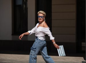 Stylish older woman running through the city in cargo jean pants with clutch and sunglasses