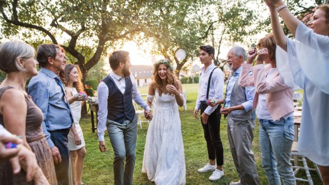 Bride and groom receiving wedding wishes from their guests at a reception outside in the backyard.