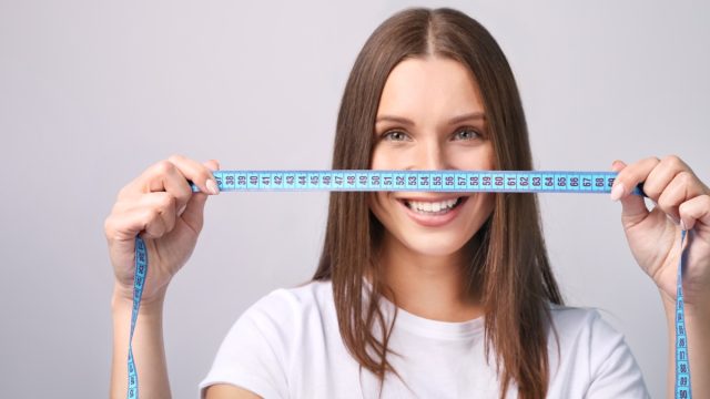 Beautiful young woman with measure tape on grey background
