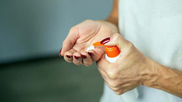 Mature woman holding bottle cream and applying moisturizing hand cream at home, Concept of health care of the hand