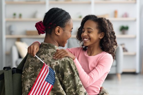 young girl hugging her mother who is wearing a camouflage military uniform