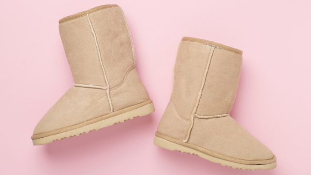 A pair of beige Ugg boots on a pink background.