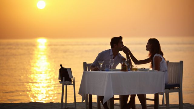 A young man kissing the hand of his wife while having dinner on the beach