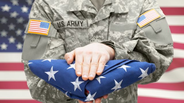 U.S. Army young soldier holding carefully folded USA flag in front of his chest