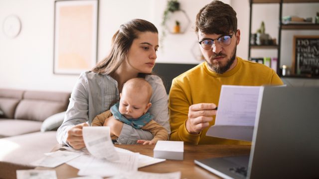 A young family sitting down at the kitchen table to pay taxes or bills on their laptop