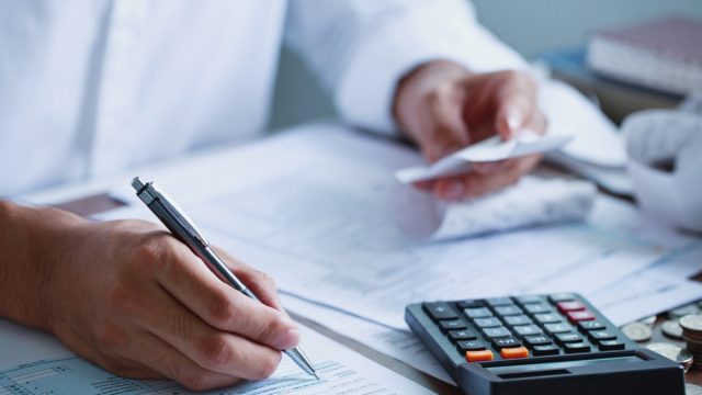 A close up of someone filling out their 1040 tax form while using a calculator