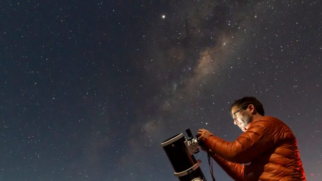 A person setting up a telescope to look at the night sky filled with stars