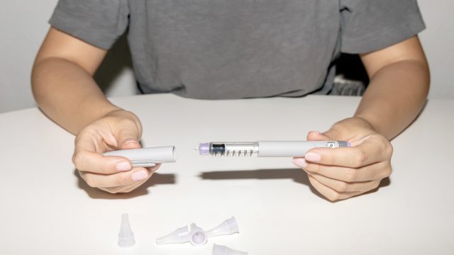 A close up of a person taking the cap off a weight loss drug injection needle