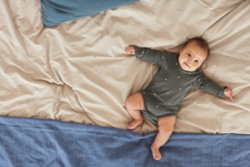 baby laying on bed in a onsie