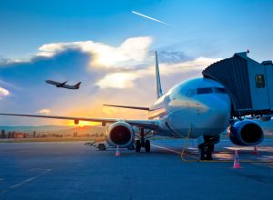 A plane sitting at the gate at an airport while a jet takes off in the background
