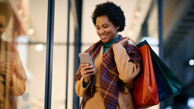Happy woman with shopping bags using mobile phone while standing in front of a store.