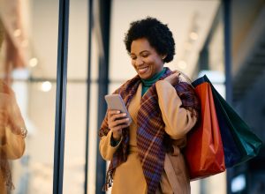 Happy woman with shopping bags using mobile phone while standing in front of a store.