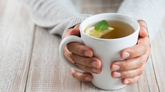 Herbal tea on wood background. Woman holding mug.