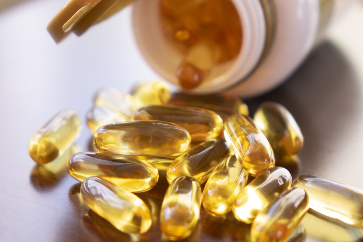 Fish oil capsules with omega 3 and vitamin D in a glass bottle on wooden texture