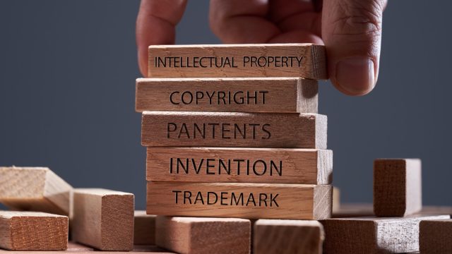 man adding a block showing the words ’Intellectual property’ on top of other wooden block with text copyright, patents, invention,and trademark