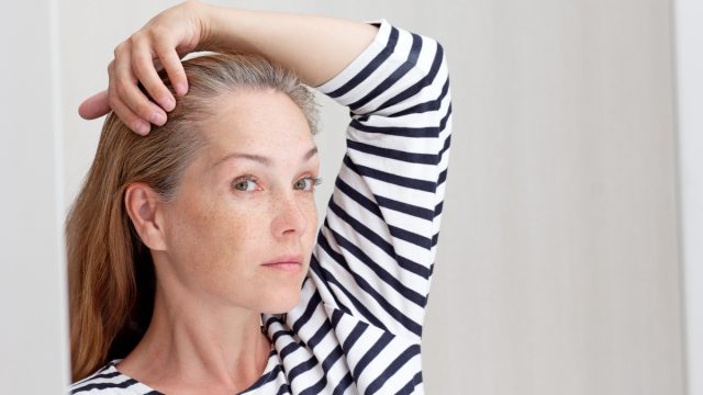 Beautiful 40s woman looking at gray hair in mirror reflection on growing out root