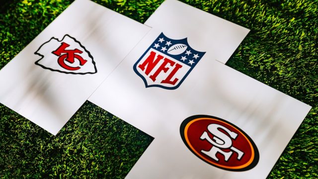 Chiefs and 49ers logos, along with an NFL logo, on white papers sitting on grass