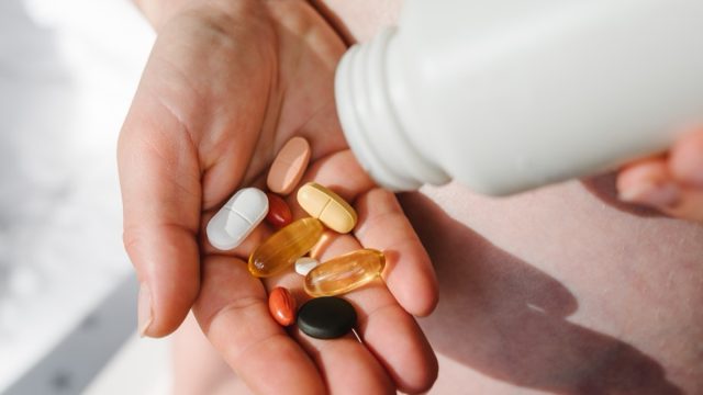Closeup photo of supplements with a white bottle. Pregnant woman take omega 3, multivitamins, vitamins B, C, D, collagen tablets, probiotics, iron capsule. Girl hold vitamins daily. Top view.