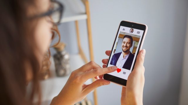 Single lady looking for boyfriend on online dating app or website. Young woman holding mobile phone, looking at profiles of male candidates and giving like to photo of handsome businessman. Crop shot