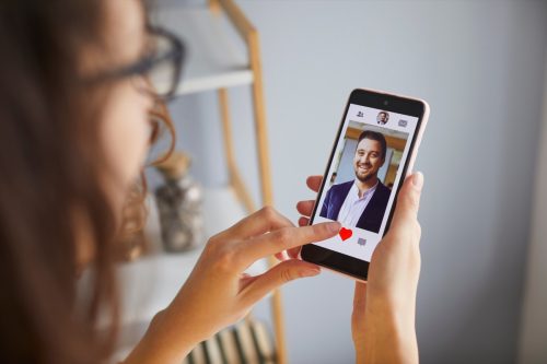 Single lady looking for boyfriend on online dating app or website. Young woman holding mobile phone, looking at profiles of male candidates and giving like to photo of handsome businessman. Crop shot