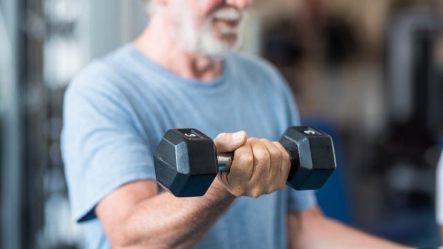 close up of mature man holding two dumbbells doing exercise at the gym to be healthy and fitness - portrait of active senior lifting weight