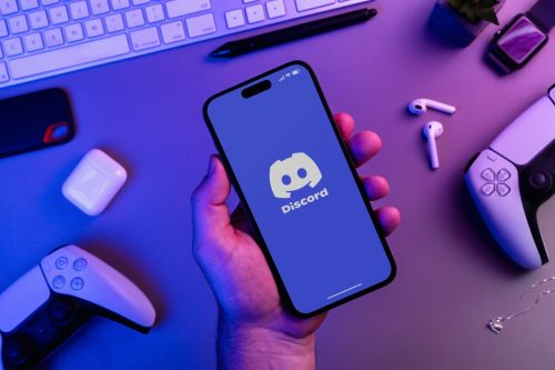 Man's hand holding an iPhone 14 Pro smartphone with Discord app