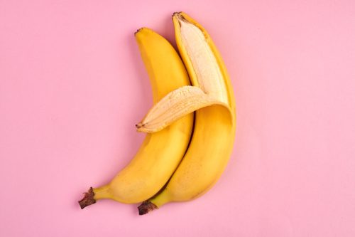 half-peeled banana resting against peeled banana against pink background
