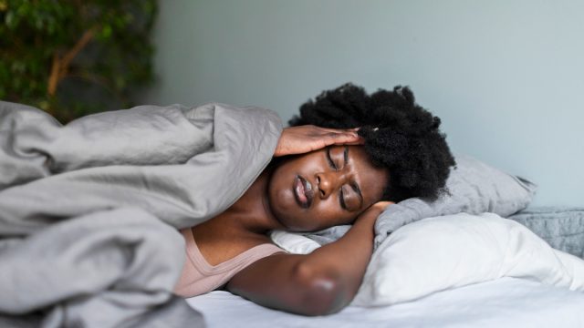 A distressed-looking woman laying in bed, holding her head, possibly having a nightmare.