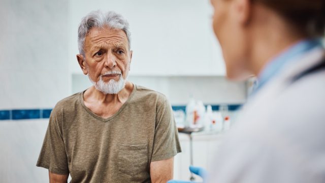 Concerned senior patient listening to his doctor after medical exam at the clinic.
