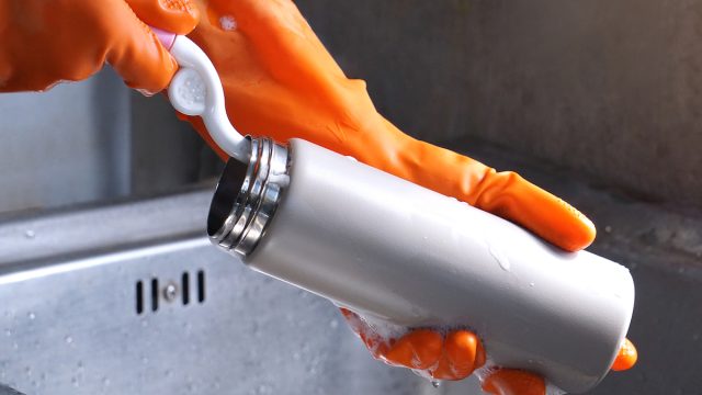 Close up of a person's hands in orange gloves washing a reusable water bottle