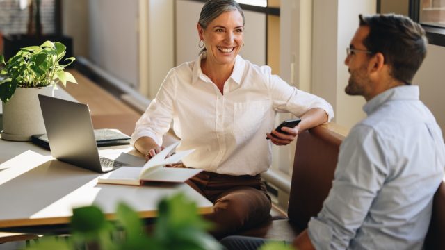 Businesswoman sitting at desk and explaining new project to coworker. Mature woman discussing working with partner in coworking office.