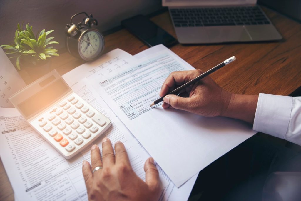 close up of man filling out tax forms with calculator