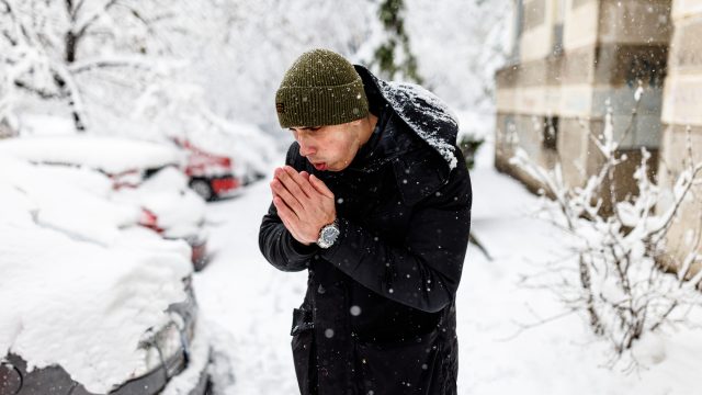 A man trying to warm his hands while standing outside in a snow storm