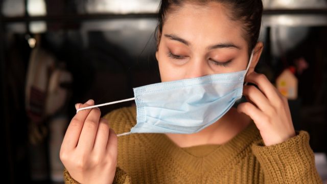 Young woman removing surgical protective face mask and for taking a deep breath and relaxed herself at home during coronavirus COVID-19, pandemic.