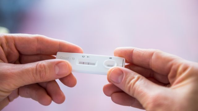 A close up of a person holding a positive COVID-19 home test