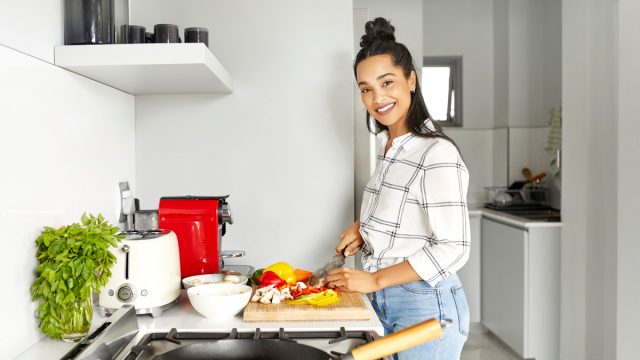 Portrait of woman cutting vegetables on chopping board. Smiling woman is preparing meal in kitchen. She is working at home.