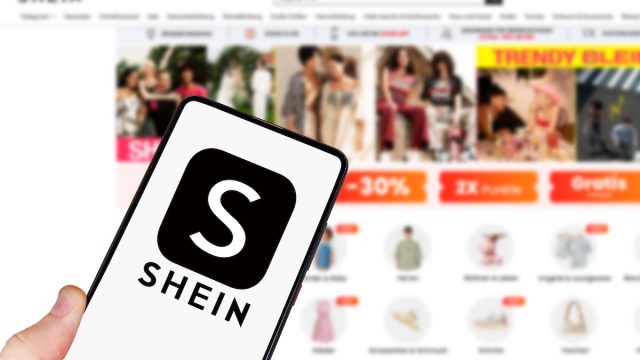 Shein logo on a smartphone in front of the website on a computer screen