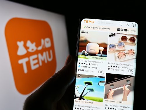 Person holding cellphone with website of Temu on screen in front of business logo. 