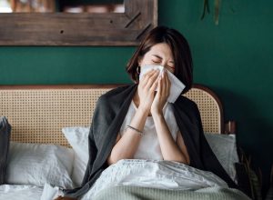 A young woman sitting in bed while blowing her nose