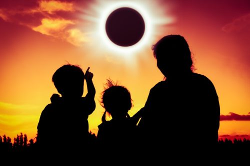 Silhouette back view of family sitting and relaxing together. Boy point to solar eclipse on gold sky background. Happy family spending time together. Outdoor.