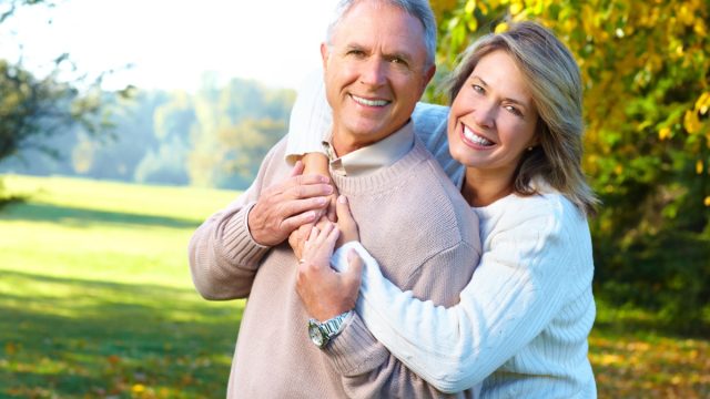 A mature mana and woman hugging and smiling at the camera while in a park
