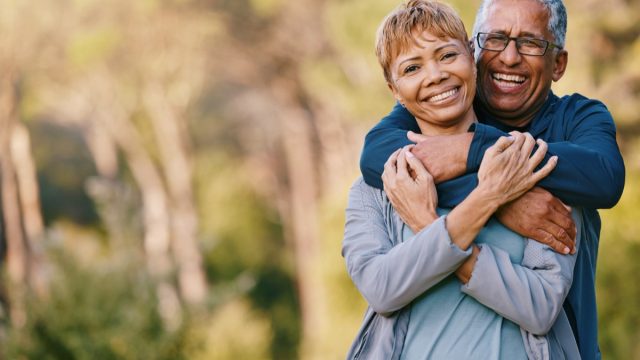 Happy Middle Aged Couple hugging outdoors with trees in the background