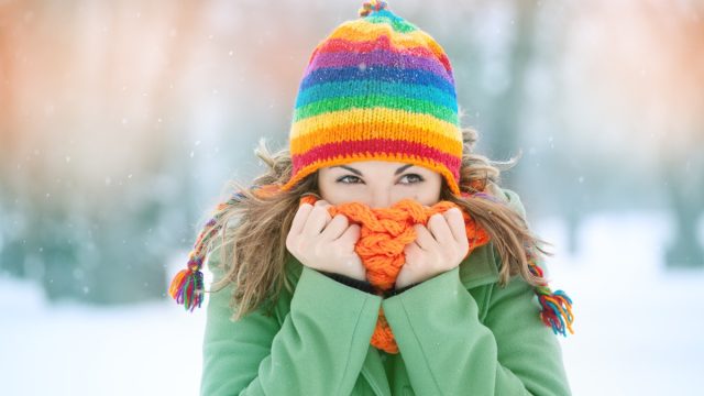 Portrait of a young woman in snow with scarf on her face trying to warm herself. Winter concept