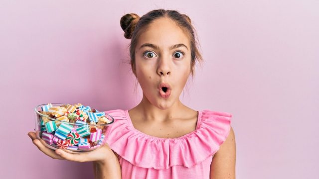 girl holding jar full of sugar candies against a pink background