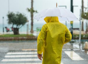 A man standing in a crosswalk in a rainstorm while wearing a raincoat and using an umbrella