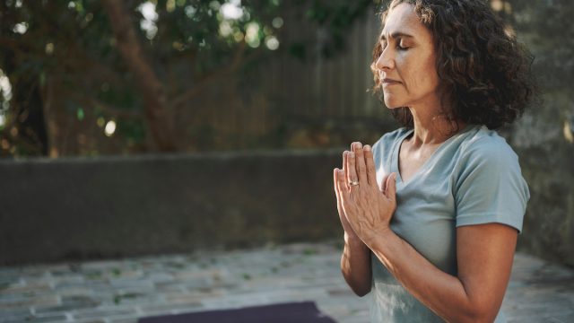 Mature woman meditating with her eyes closed on an exercise mat during a yoga session outside in a courtyard