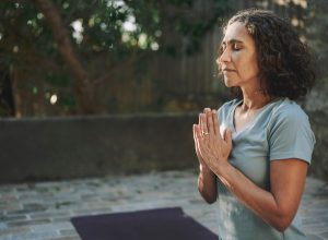 Mature woman meditating with her eyes closed on an exercise mat during a yoga session outside in a courtyard