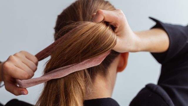 Young woman doing a ponytail with velvet hair tie, scrunchie, view from the back